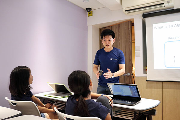 Man standing in front of a projector talking to two female students