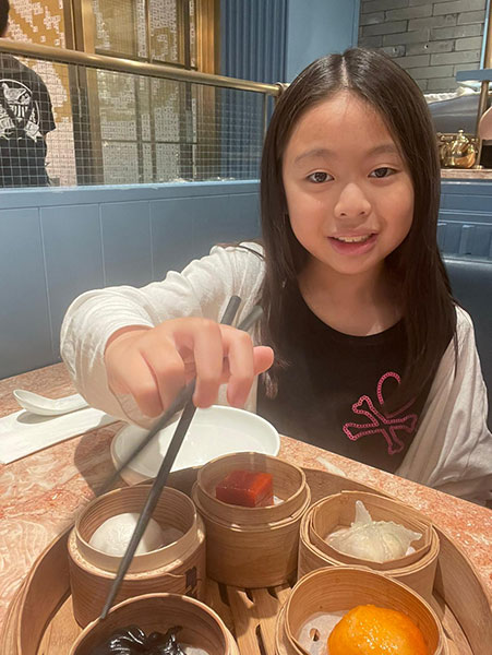9 year old Asian girl holding chopsticks and smiling at camera